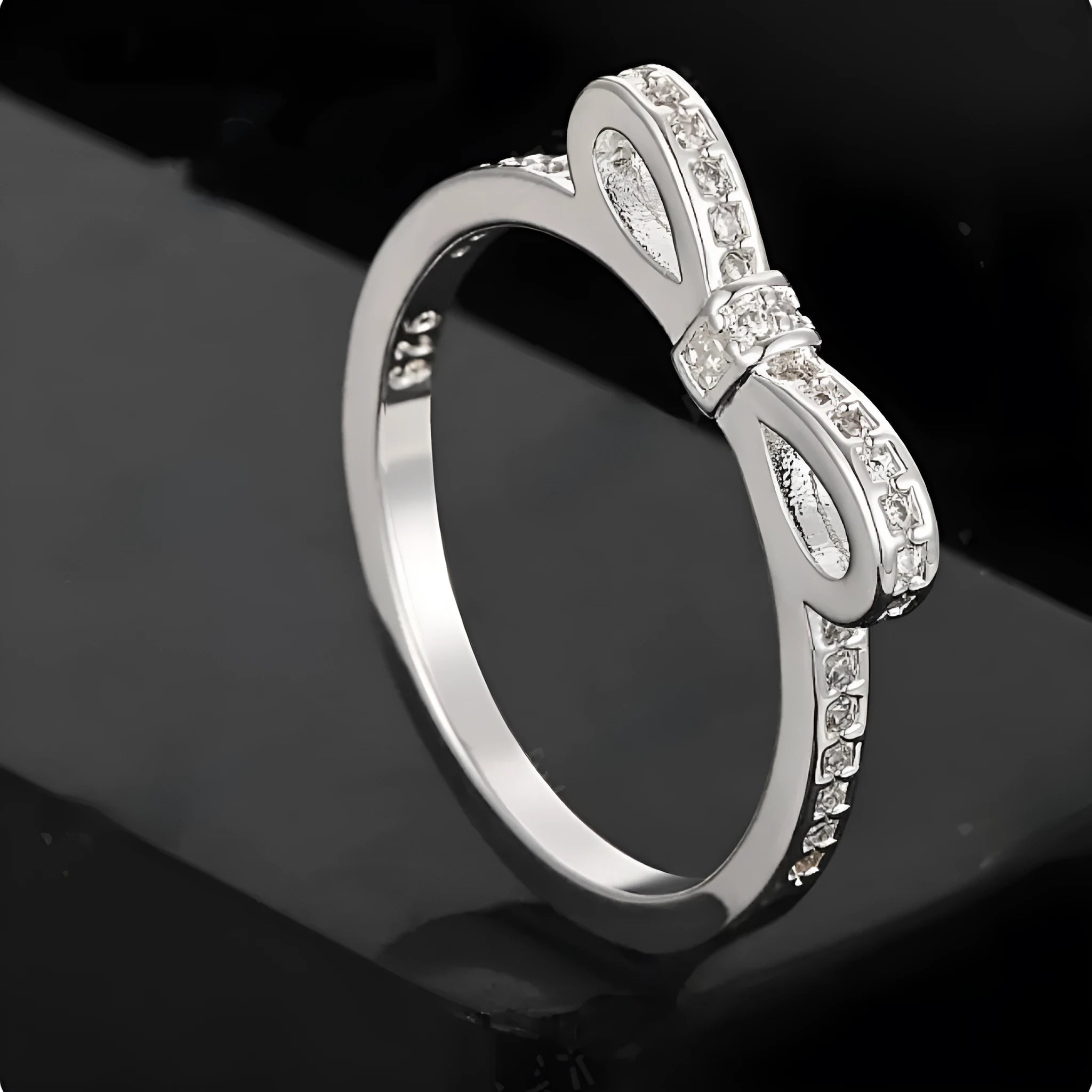 Silver bow-shaped ring with sparkling rhinestones and zircon crystals on a finger.