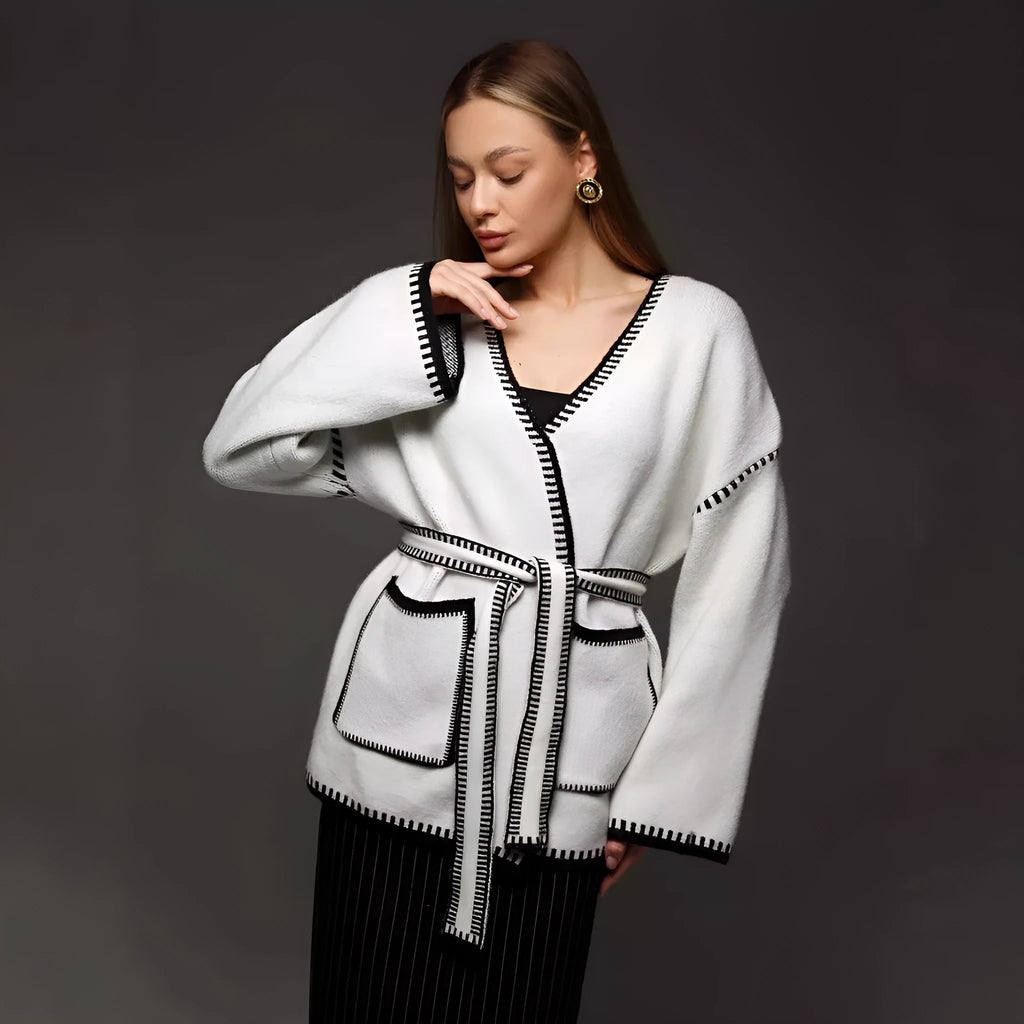 A white lace-up knitted cardigan with long sleeves on a hanger, showing the front tie detail.