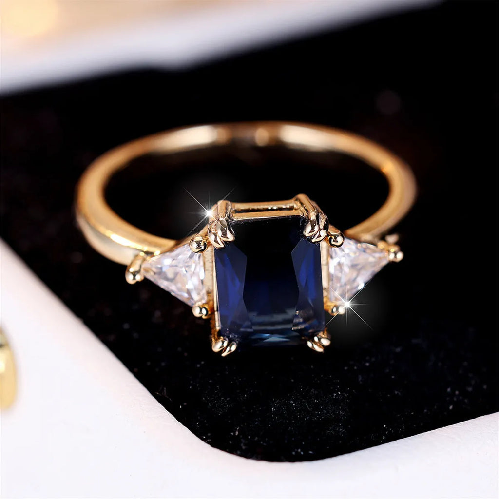 A rectangular gold sapphire blue plated copper ring for women on a plain background.