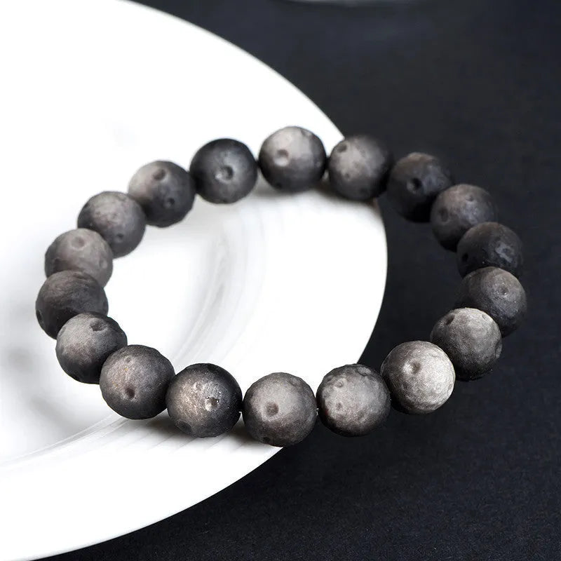 Natural obsidian crater ball bracelet with textured beads on a wrist, showing silver stone meteorite colour variant.