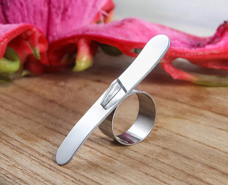 Silver stainless steel finger ring fruit peeler for oranges and pomelos on a kitchen surface.