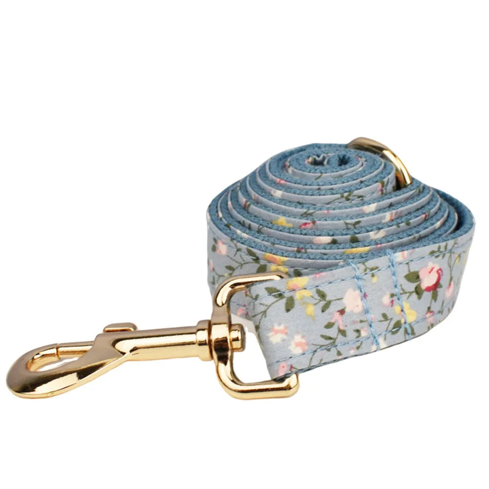 Blue floral patterned dog collar and matching leash, bow, vest, and poop bag set on a white background.
