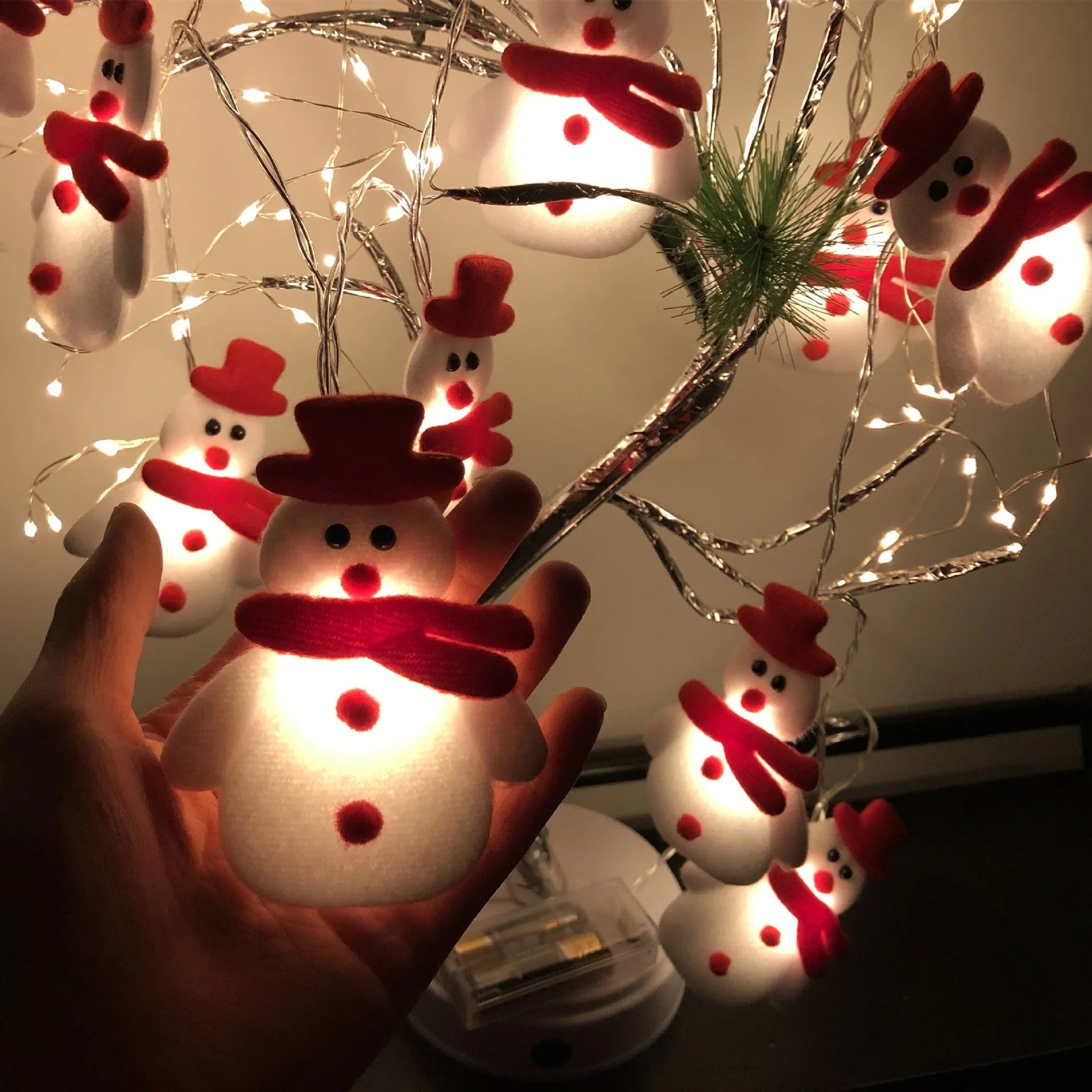 Snowman and elk deer decorative LED Christmas string lights glowing warm white on a green garland.