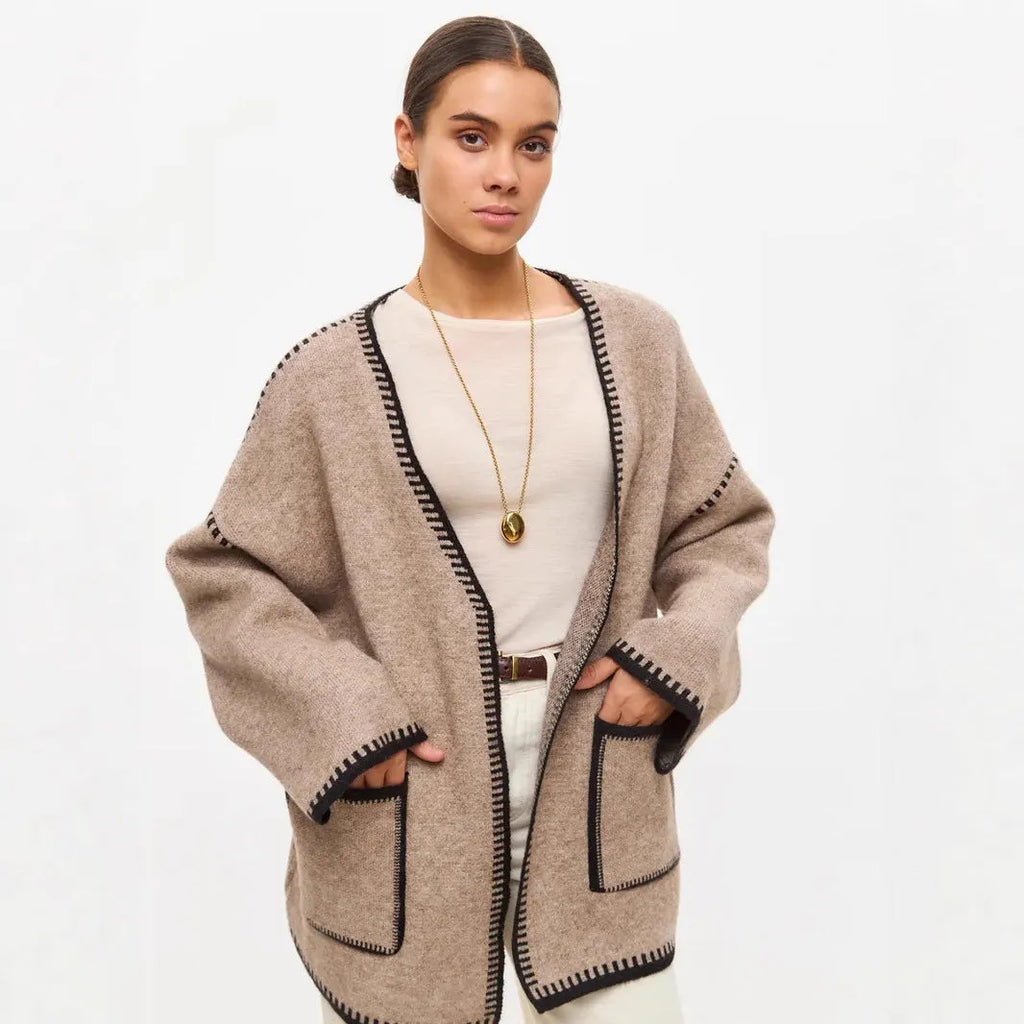 A white lace-up knitted cardigan with long sleeves on a hanger, showing the front tie detail.