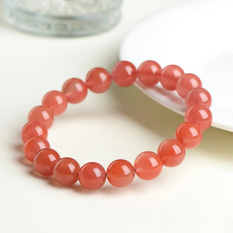 Natural cherry red agate bracelet with polished beads in a scattered design on a wrist.