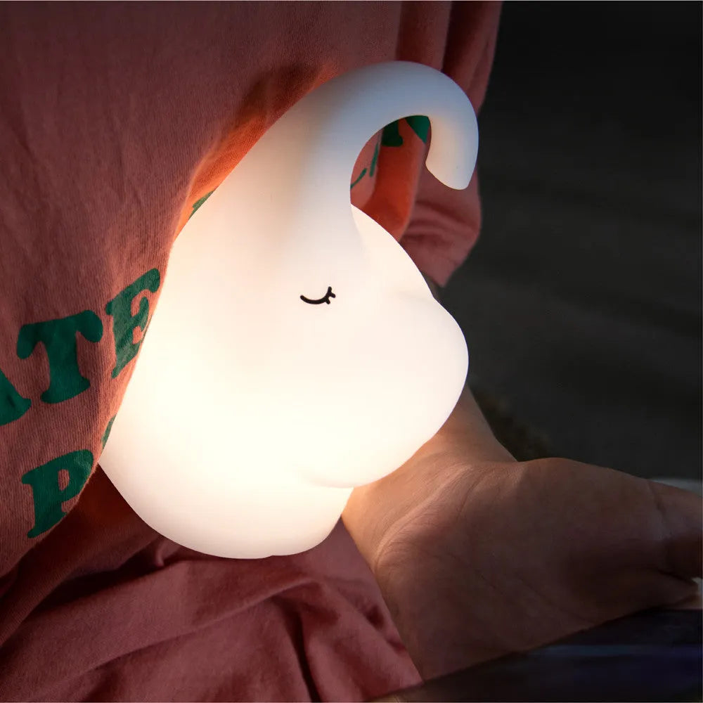 White elephant silicone night light with warm glow on a bedside table.