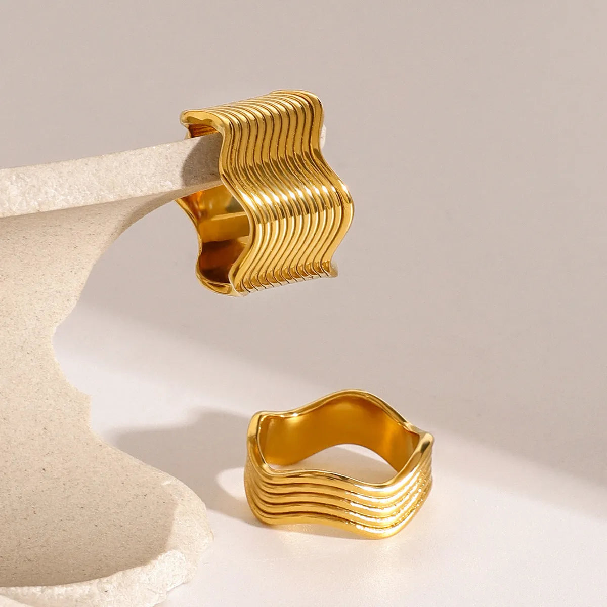 Close-up of a wide stainless steel ring with a geometric wave texture, shown in a silver tone finish.