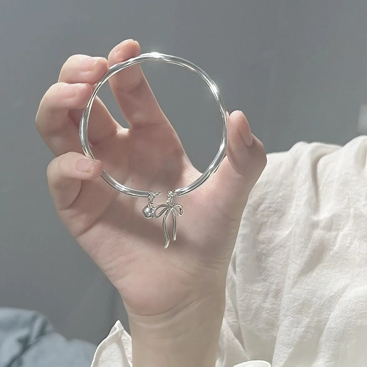 Adjustable silver women's bracelet with a bow bell charm on a white background.
