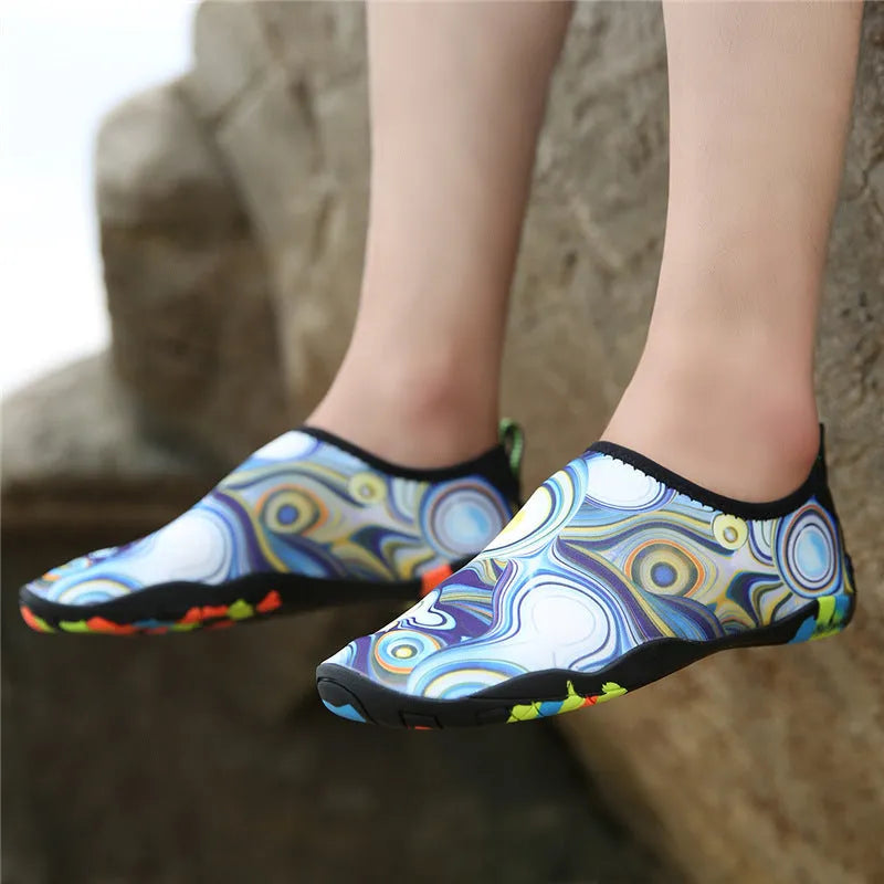 Blue and black Lycra fabric beach wading shoes with EVA foam soles on a sandy background.