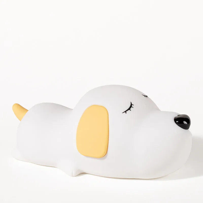 Soft silicone cartoon dog night light with USB cable on a bedside table.