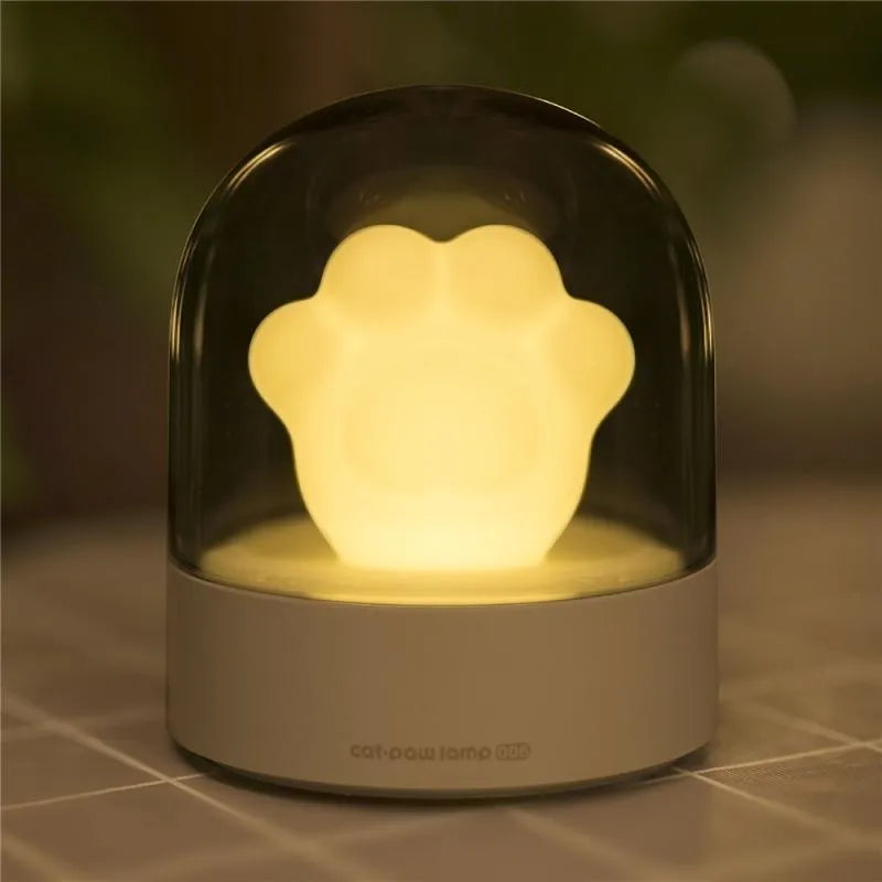 Cute grey or pink cat paw shaped USB rechargeable night light with music box on a desk.
