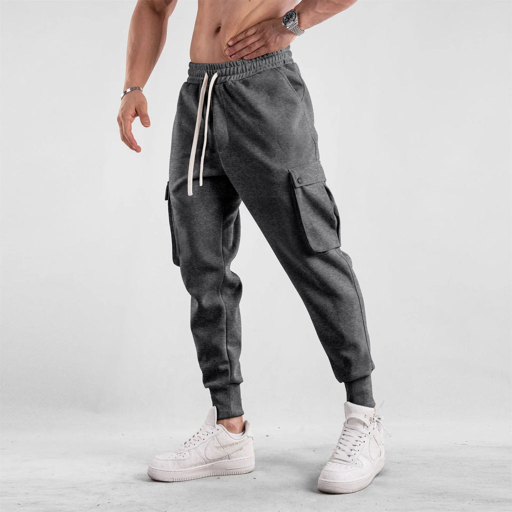 Men's loose-fit beige cotton sports trousers with ankle ties and side pockets laid flat.