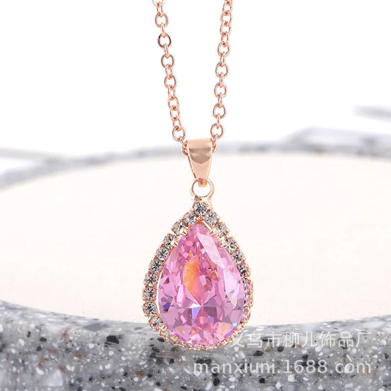 Close-up of a women's rose gold tone drop pendant necklace with pink rhinestone inlay on a model.