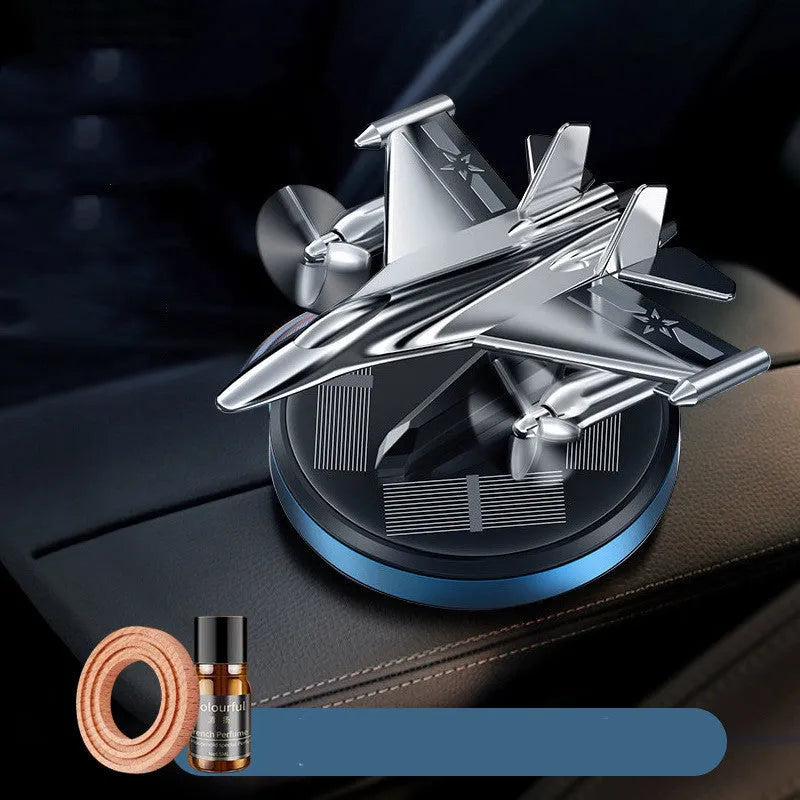 Silver solar powered rotating fighter jet perfume ornament on a car dashboard.