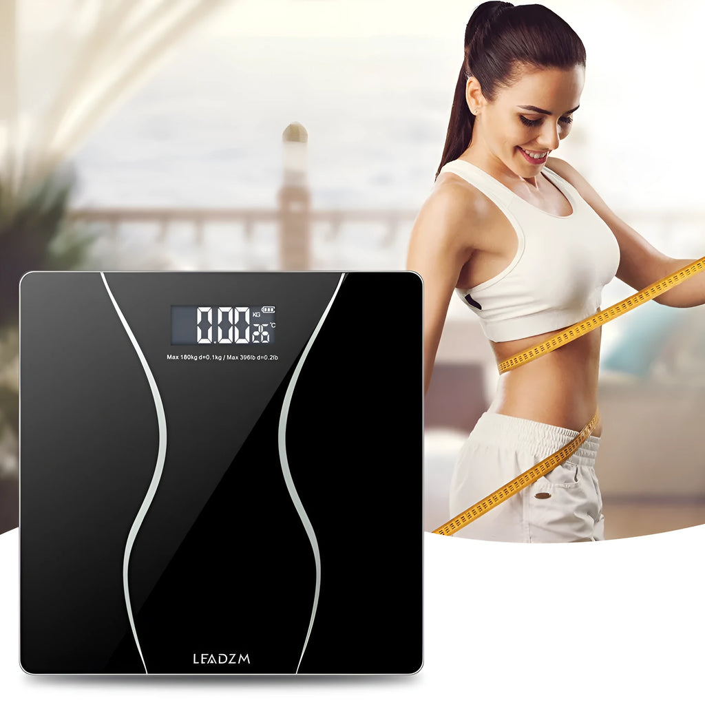 Black electronic digital body scale on a floor with a 180kg maximum capacity.