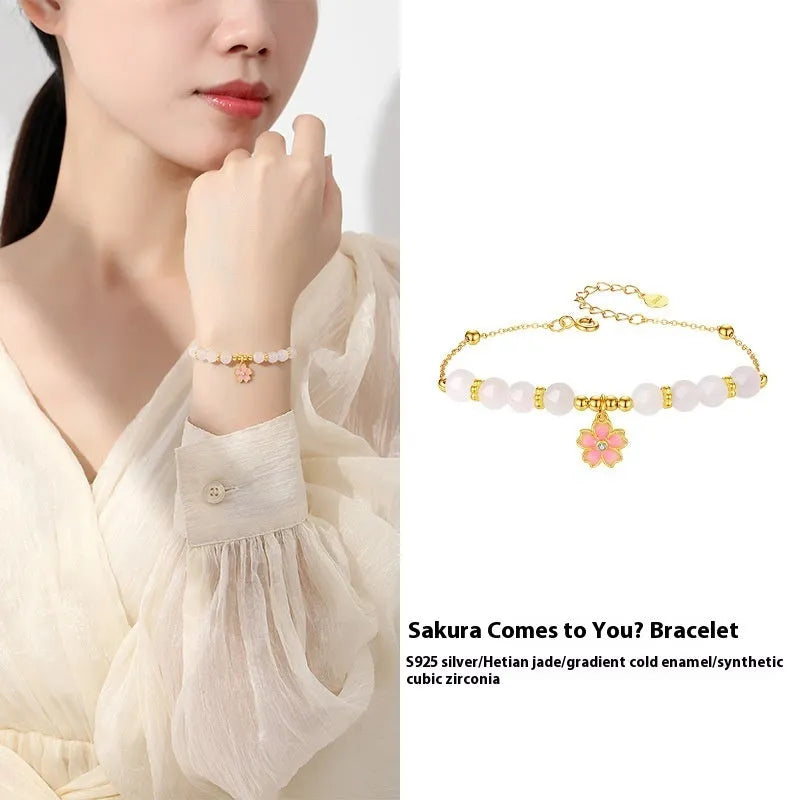 Close-up of a women's pink cherry blossom pendant and Hetian jade bead bracelet made from S925 silver.