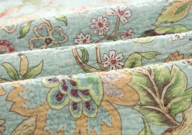 Blue American-style floral and bird quilted cotton bedspread set on a bed, showing its 230x250 cm size.