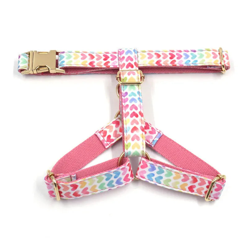 Pink colourful dog harness with gold buckle and heart-shaped stone decoration on a white background.