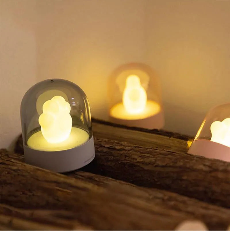 Cute grey or pink cat paw shaped USB rechargeable night light with music box on a desk.