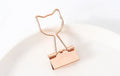 Gold metal decorative paper clips in shapes of a flamingo, a cat, a cactus, a bow, a love symbol, and clouds.