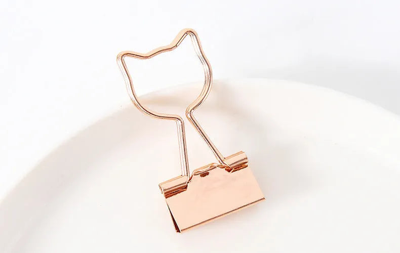 Gold metal decorative paper clips in shapes of a flamingo, a cat, a cactus, a bow, a love symbol, and clouds.