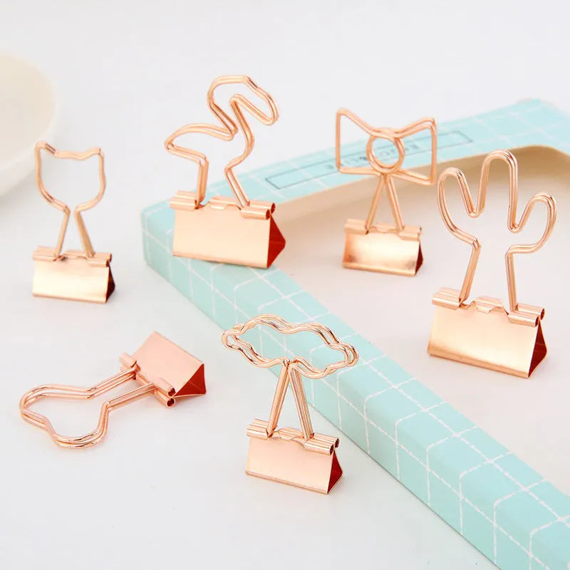 Gold metal decorative paper clips in shapes of a flamingo, a cat, a cactus, a bow, a love symbol, and clouds.