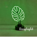 Minimalist bamboo-shaped white desk lamp with green glowing tube on a wooden table.