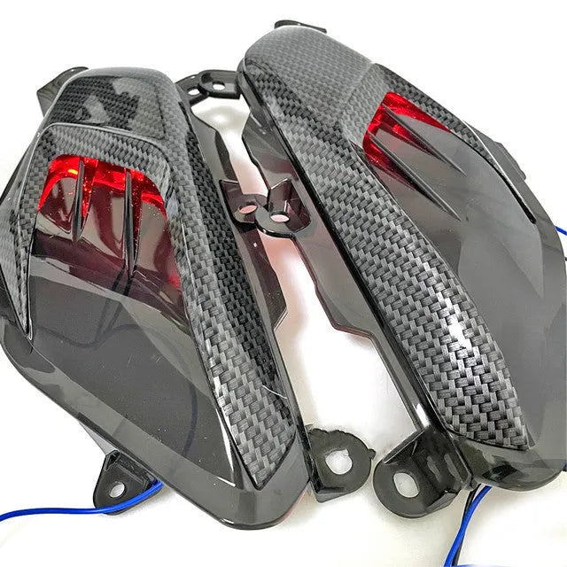 Pair of Yamaha NMAX side lamps with LED light and carbon fibre decoration on a black background.