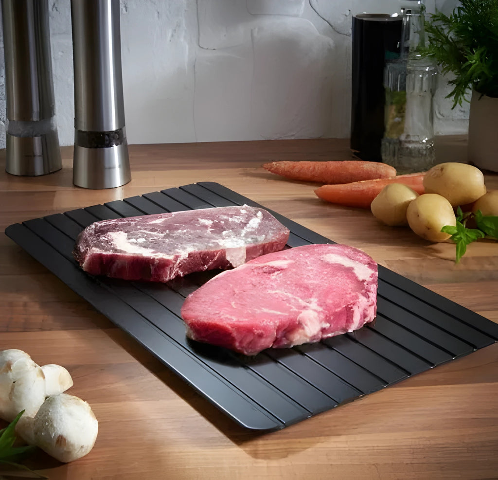 Black aluminium quick defrosting tray for thawing meat and frozen food on a kitchen counter.