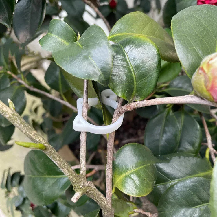 Green plastic cat-shaped plant clip holding a vine against a wooden stake.