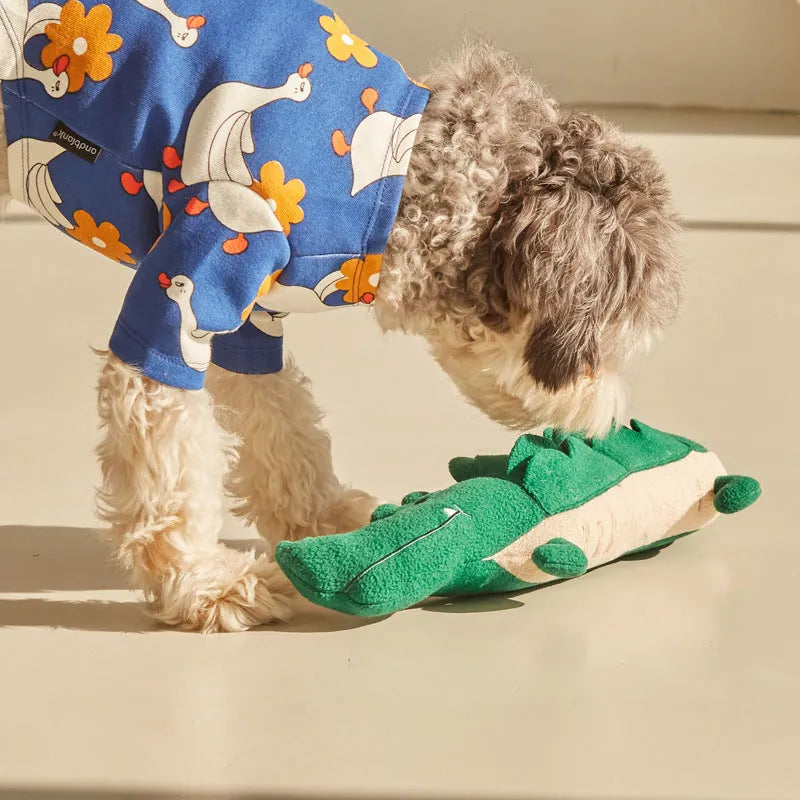 Green soft plush toy dog with floppy ears and embroidered face, lying on a white background.