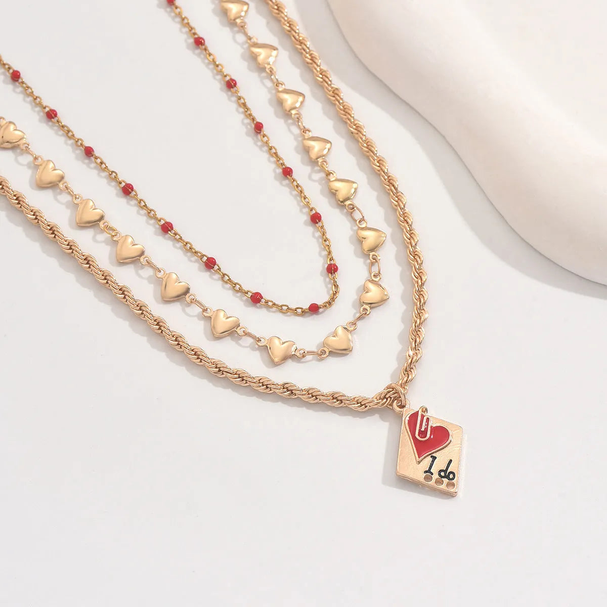 Close-up of a silver-toned three-layer necklace with small geometric heart pendants on an adjustable chain.
