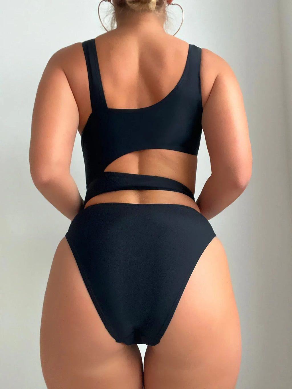 Black hollow high cut one-piece swimsuit on hanger showing sleeveless design