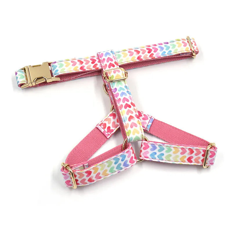 Pink colourful dog harness with gold buckle and heart-shaped stone decoration on a white background.