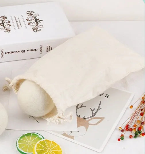 A natural wool drying ball for tumble dryers next to a plain cotton storage bag on a laundry background.