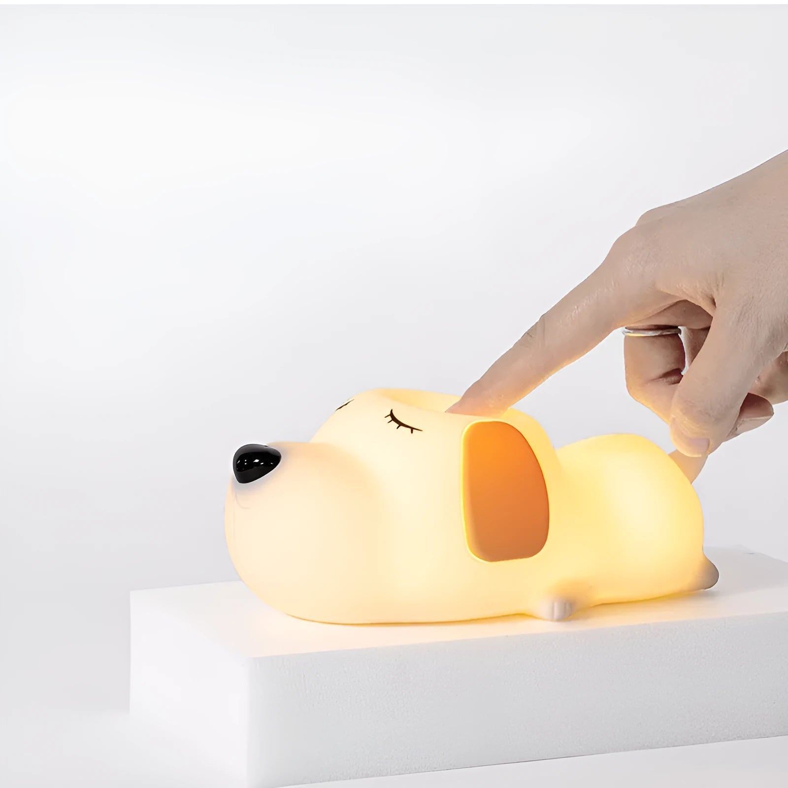Soft silicone cartoon dog night light with USB cable on a bedside table.