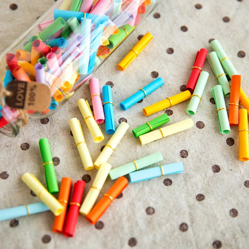 Assorted colourful mini paper scrolls with metal eyelets, shown in 3x7cm, 4x7cm and 5x5cm sizes