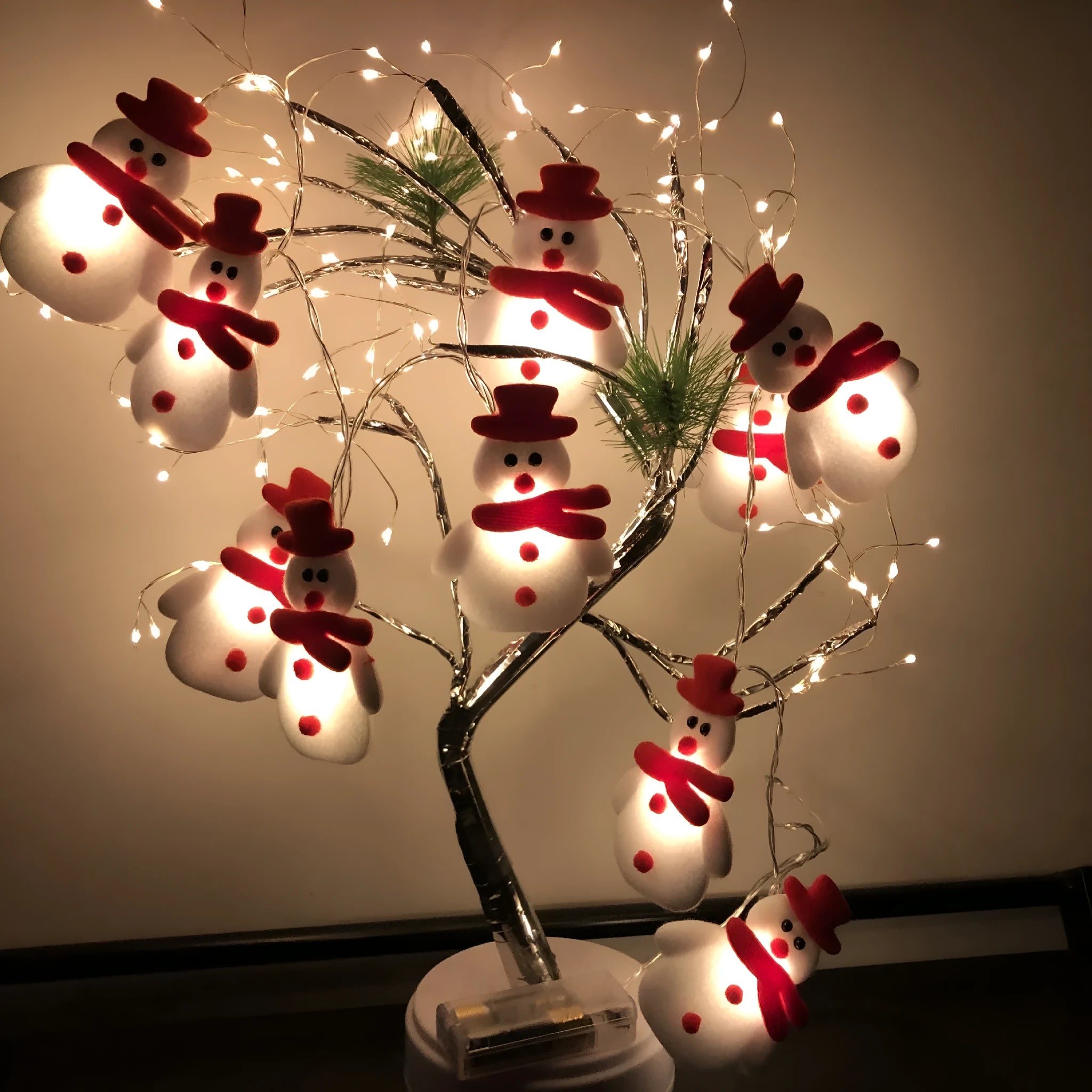 Snowman and elk deer decorative LED Christmas string lights glowing warm white on a green garland.