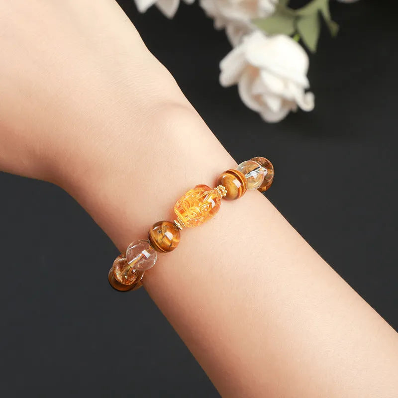 Close-up of a yellow tiger's eye and citrine bead bracelet with a geometric pi xiu charm on a wrist.