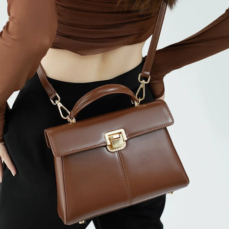 Women's black leather shoulder bag with vachette clasp showing interior zippered compartments