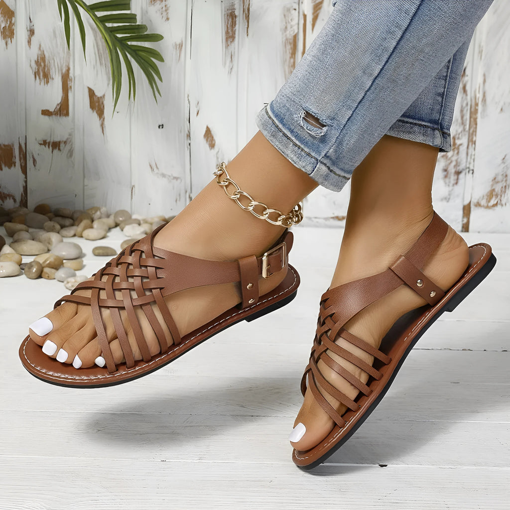 Black flat buckle open toe Roman style cross strap beach slippers on a plain background.