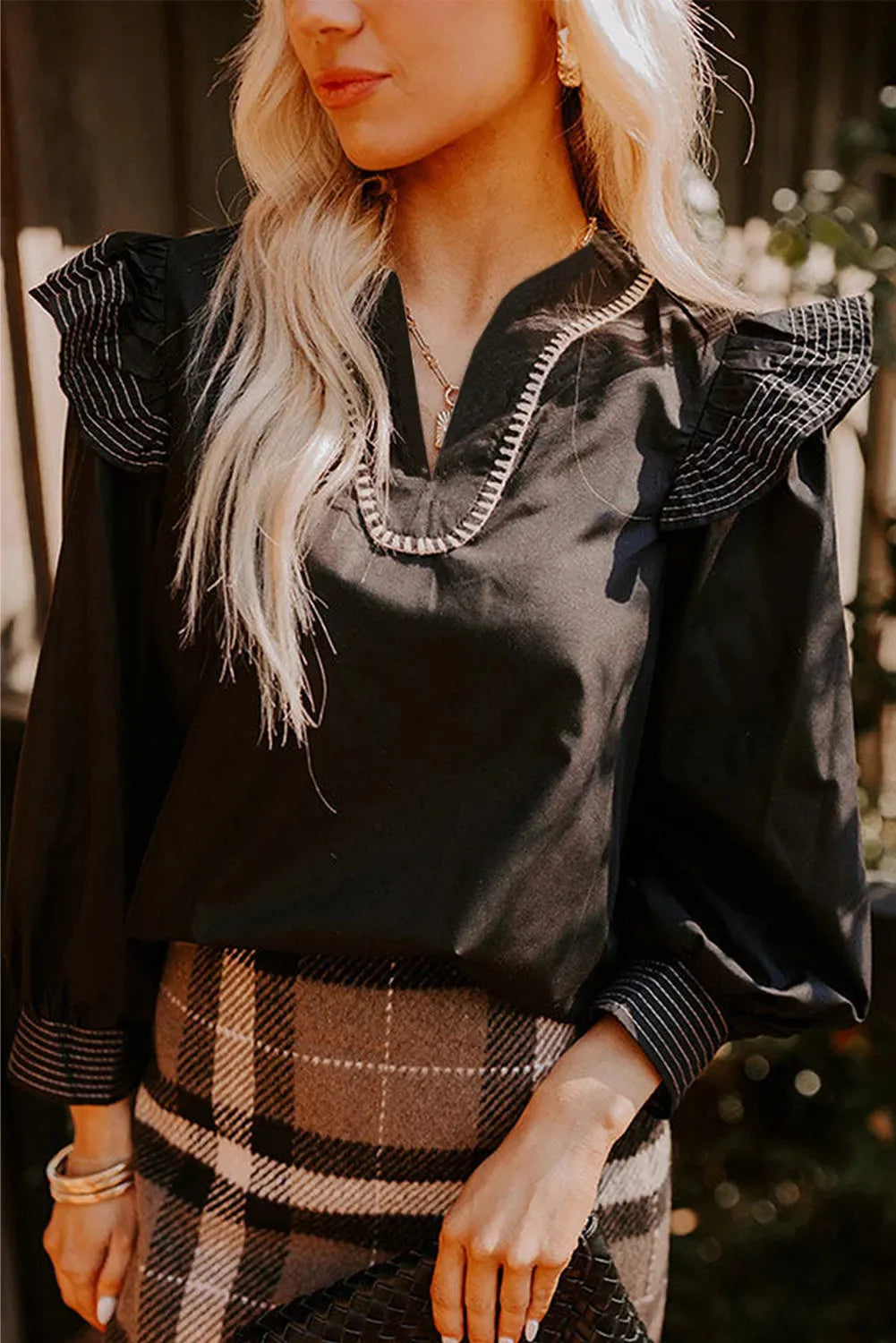 Black V-neck long sleeve blouse with a decorative ruffle and contrast stitching.