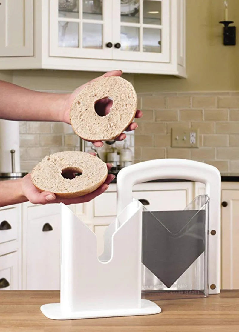 White plastic bagel slicer with acrylic safety shield and stainless steel serrated blade on a kitchen counter