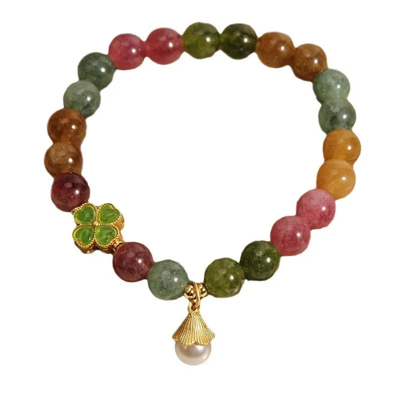 Close-up of a women's silver-toned bracelet with a four-leaf clover charm, pearl pendant, and colourful tourmaline stones.