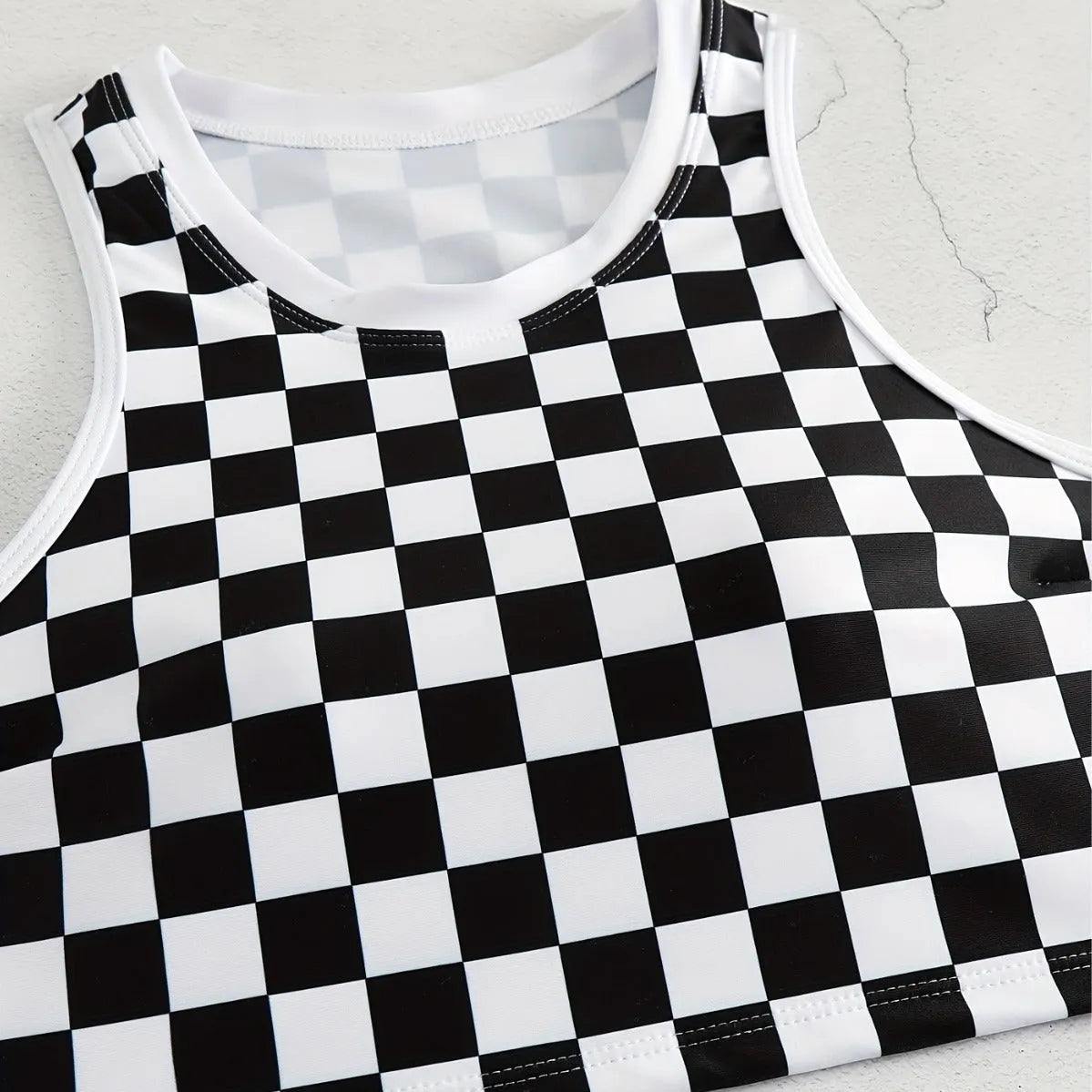 Backless one-piece women's swimsuit with black and white chessboard plaid pattern and white suspender straps.