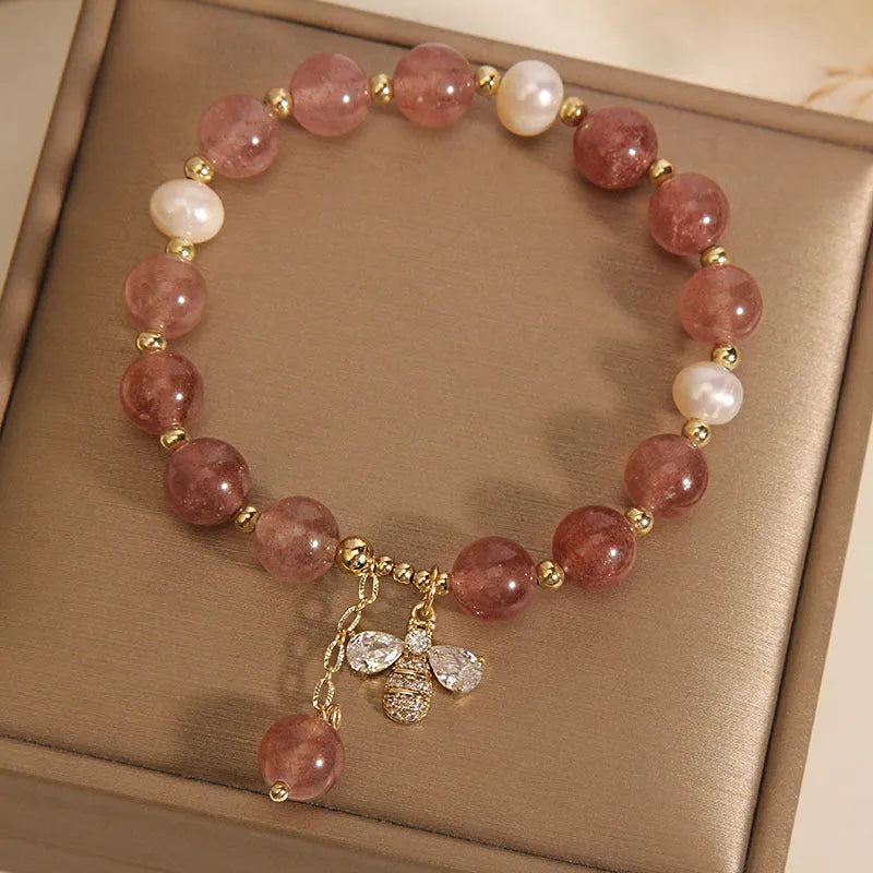 Women's bracelet with strawberry quartz pearls, a zircon bee charm, and alloy links on a wrist.