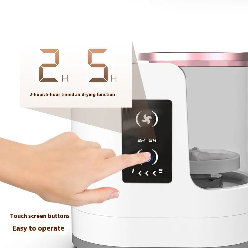 White electric makeup brush cleaner with drying chamber on a table, next to makeup brushes.