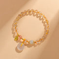 Gold rutilated quartz bracelet with geometric safety buckle and pendant on a white background.