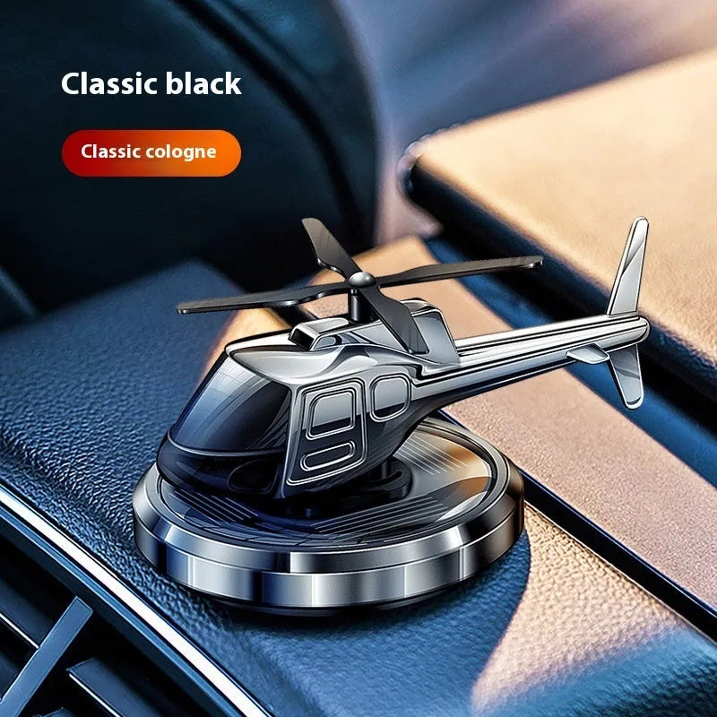 Silver solar-powered metal helicopter car air freshener with rotating blades on a dashboard.