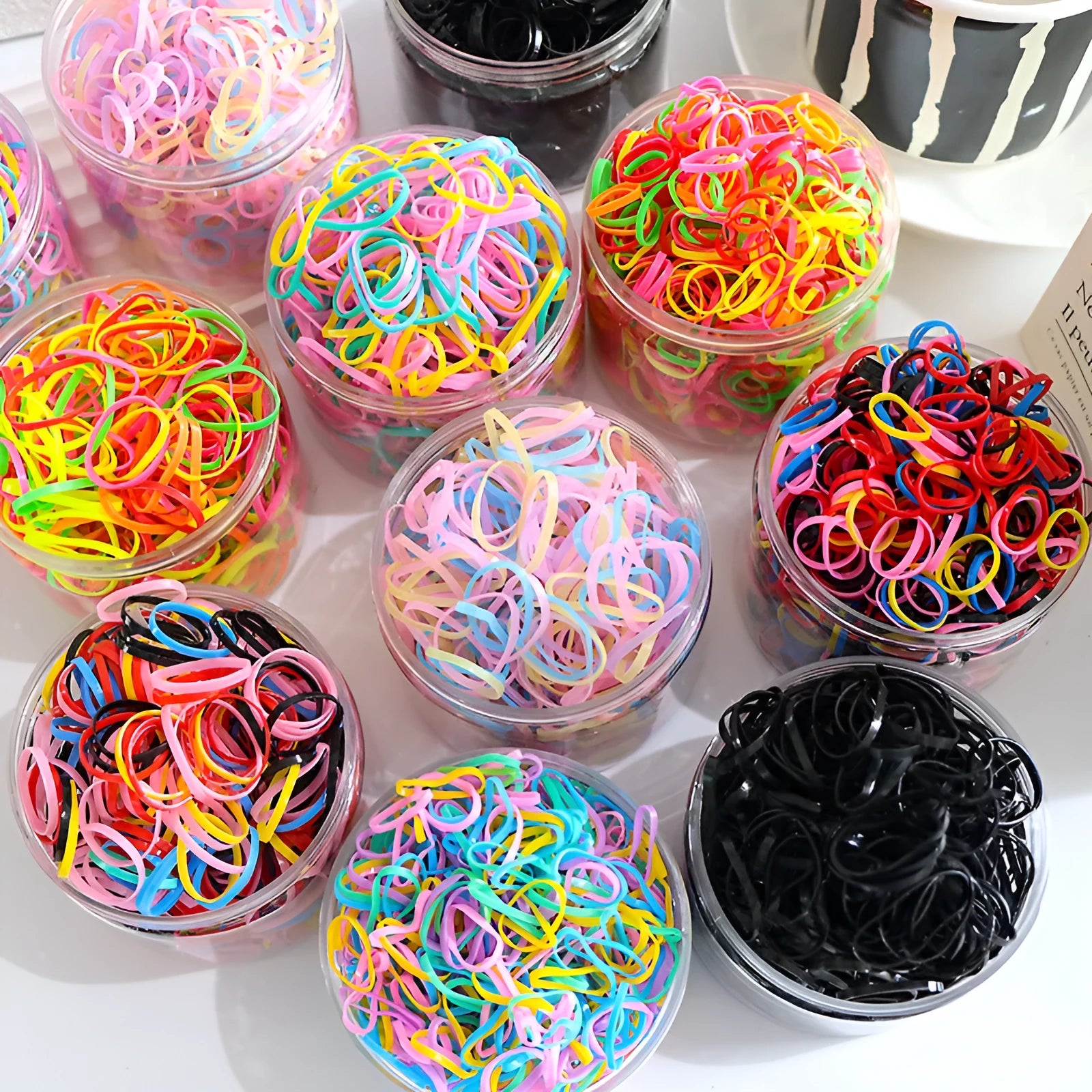 Pack of multicoloured thin TPU baby hair ties for toddlers in a reusable clear storage container.